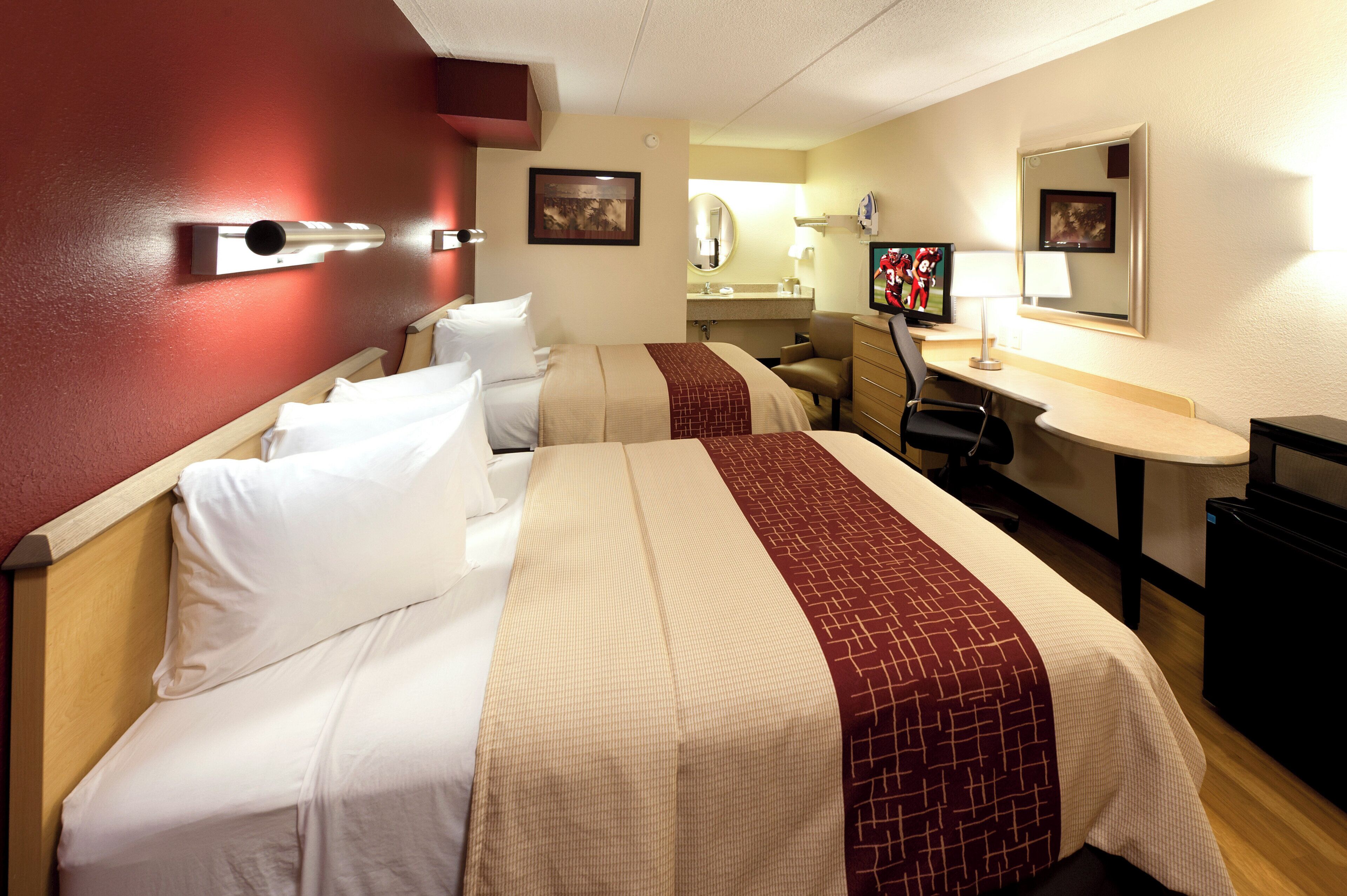 A hotel room with two beds, a desk, a chair, a television, and a mirror.