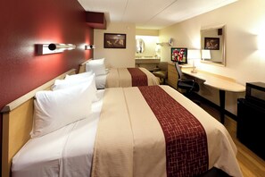 Ein Hotelzimmer mit zwei Betten, einem Schreibtisch, einem Sessel, einem Fernseher und einem Spiegel.
