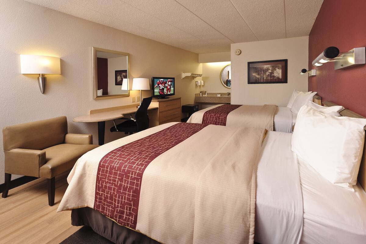 Une chambre d’hôtel avec deux lits, un bureau, une chaise, une télévision et un miroir.
