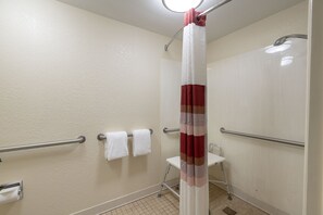 Ein Badezimmer mit Duschvorhang, Haltegriffen, einer weißen Toilette und einem Handtuchhalter mit zwei Handtüchern.