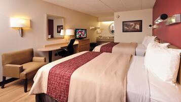 A hotel room with two beds, a desk, a chair, a television, and a bathroom.