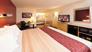 A hotel room with a large bed, a desk with a chair, a television, a mirror, and a small kitchenette.