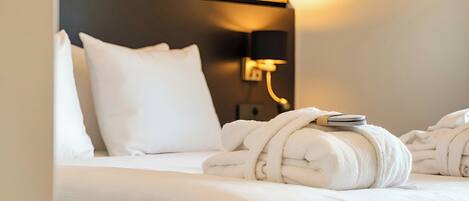 A hotel room with a neatly made bed, a wall-mounted lamp, and a towel rack with towels.