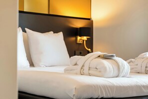 Een hotelkamer met een net opgemaakt bed, een wandlamp en een handdoekrek met handdoeken.