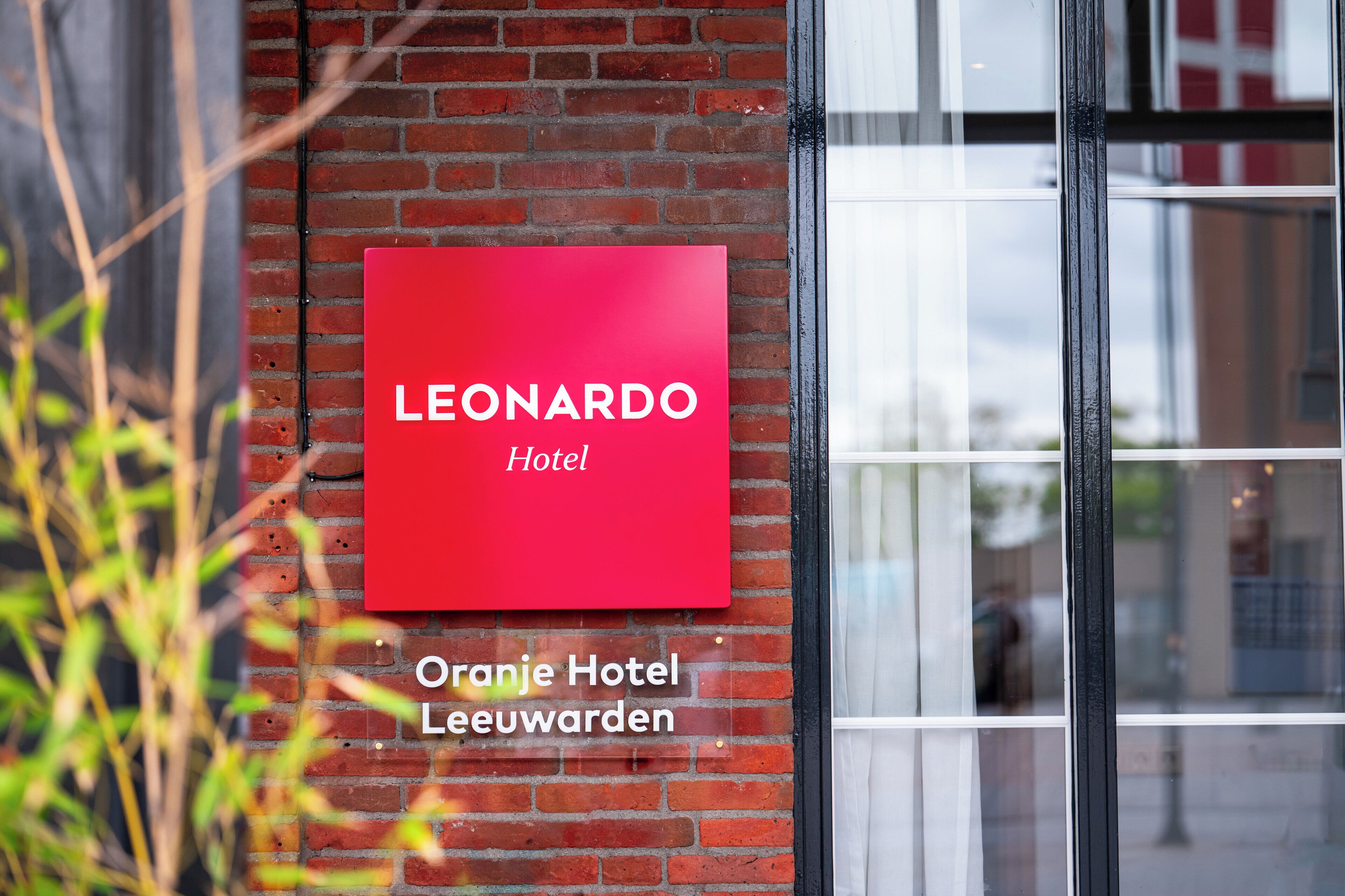 Un letrero rojo con la inscripción "LEONARDO Hotel" y "Oranje Hotel Leeuwenwaarden" sobre una pared de ladrillo.