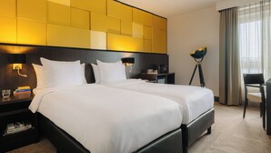 A hotel room with two beds, a desk, a chair, and a lamp.