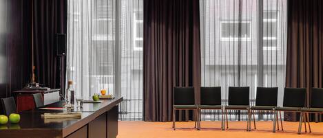 A conference room with a long table, four chairs, a speaker, and a window with curtains.