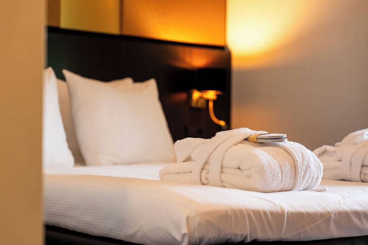 Una cama bien hecha con sábanas blancas y una toalla blanca enrollada encima.