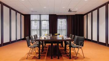 Een congreszaal met een grote tafel, stoelen en een projectiescherm.