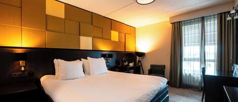 Una habitación de hotel con una cama grande, mesitas de noche, un escritorio y una lámpara.