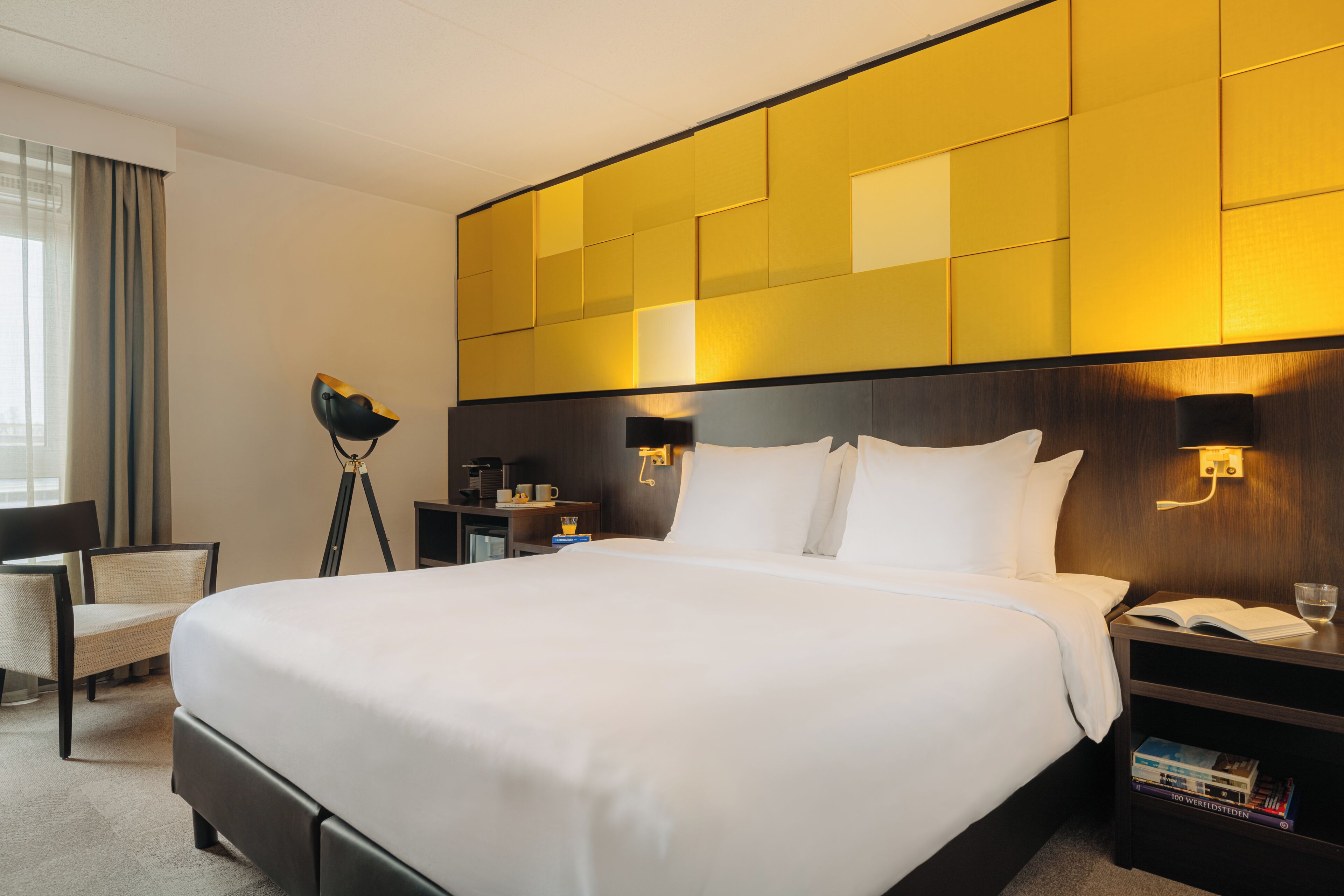 A hotel room with a large bed, bedside tables, a chair, and a desk with a lamp.