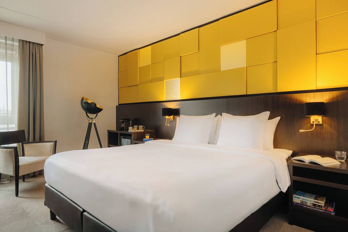 Habitación de hotel con una cama grande, mesitas de noche, una silla y un escritorio con lámpara.