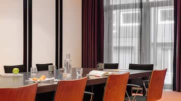 A conference room with a long table, chairs, a water bottle, a glass, a book, and a fruit plate.