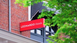 A red sign with "Leonardo Hotels" written on it, mounted on a brick building with windows.