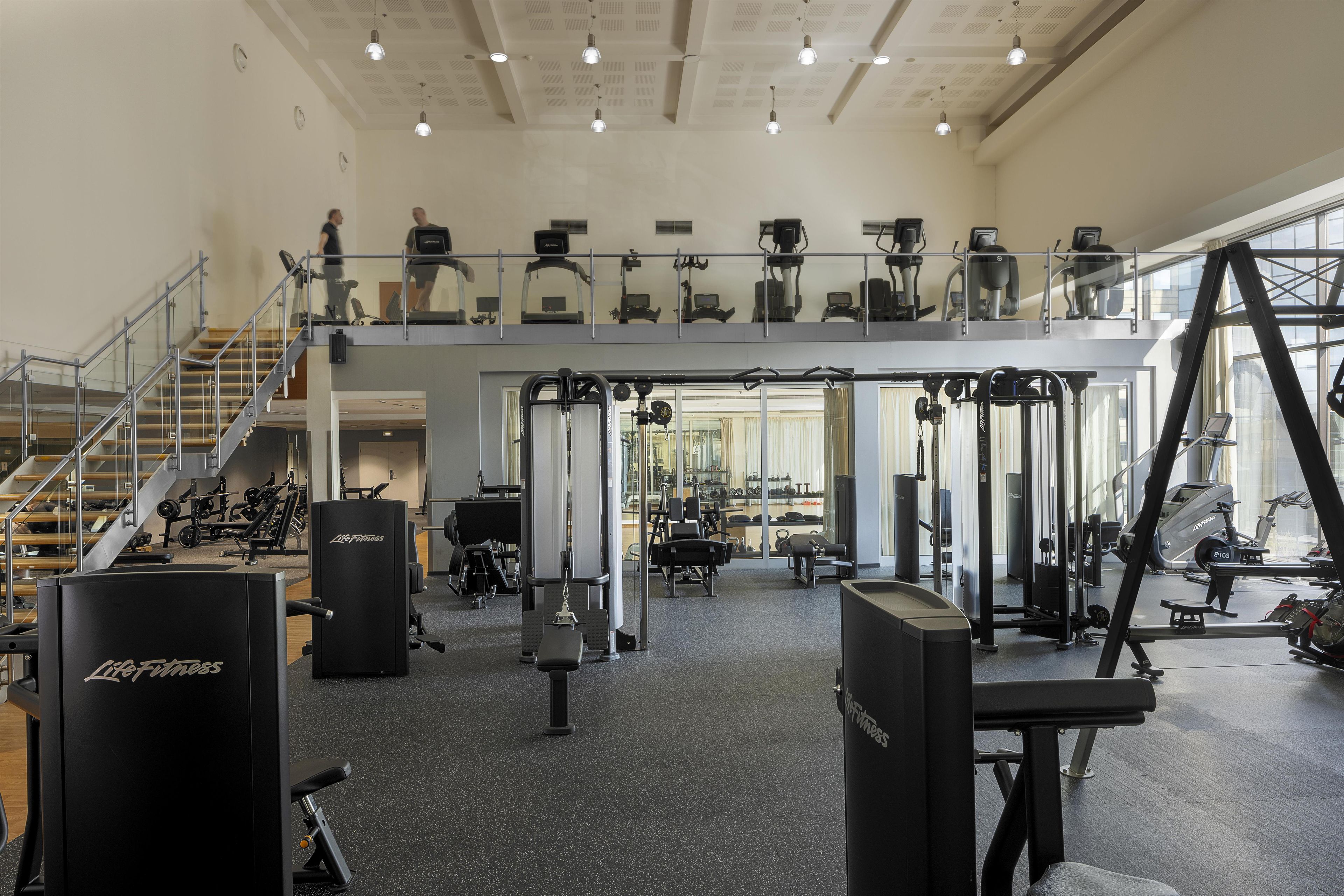 Una palestra su più livelli con diverse attrezzature per esercizi, una scala e un soppalco con macchinari cardio.