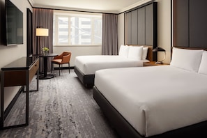 A hotel room with two beds, a desk, a chair, a TV, and a window with curtains.
