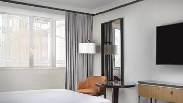 A hotel room with a bed, a chair, a desk, a mirror, and a television.