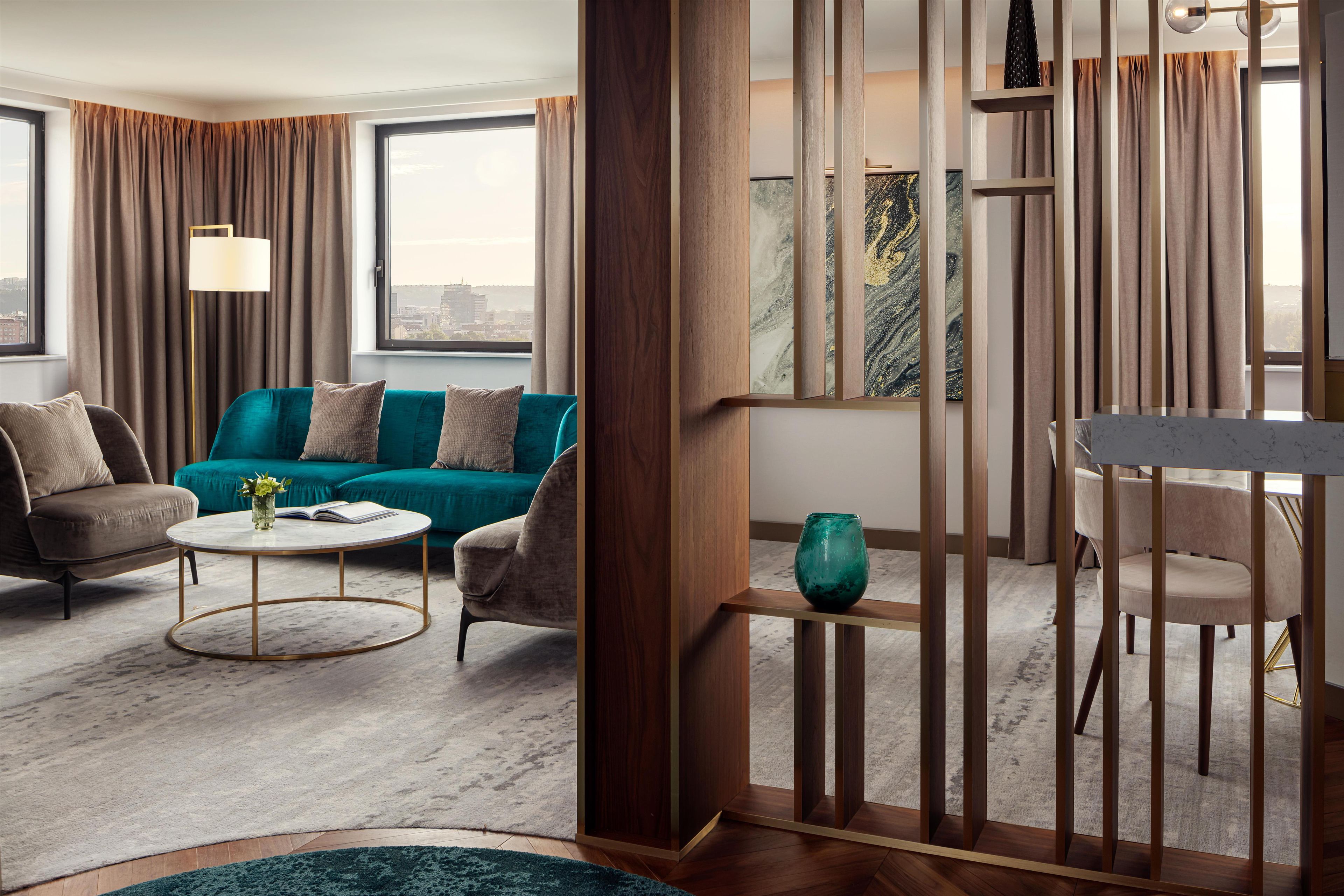 A modern living room with a teal sofa, a round coffee table, and a view of the city through large windows.
