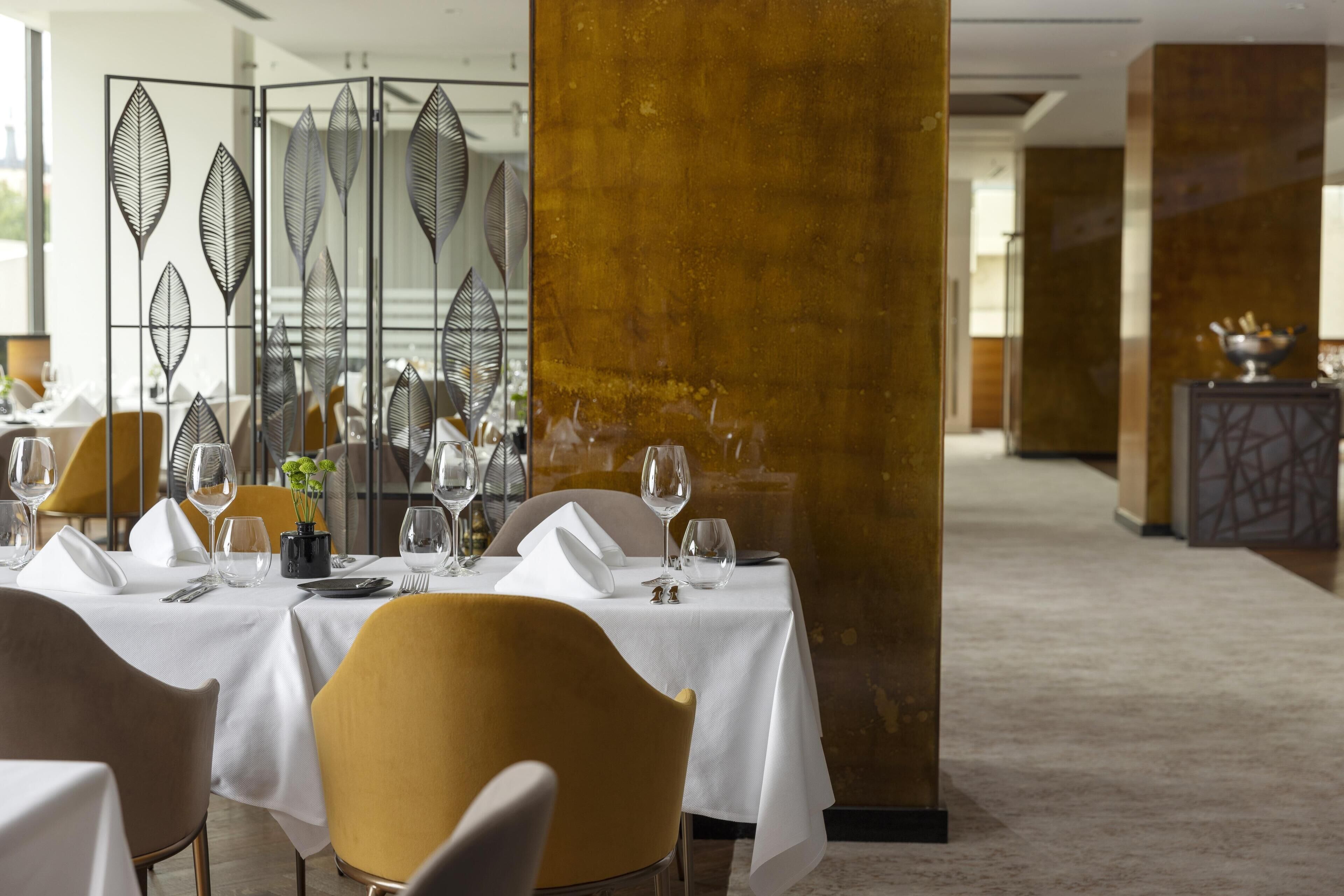 Un restaurante con mesas dispuestas para comer, un separador decorativo y una columna con superficie texturizada.