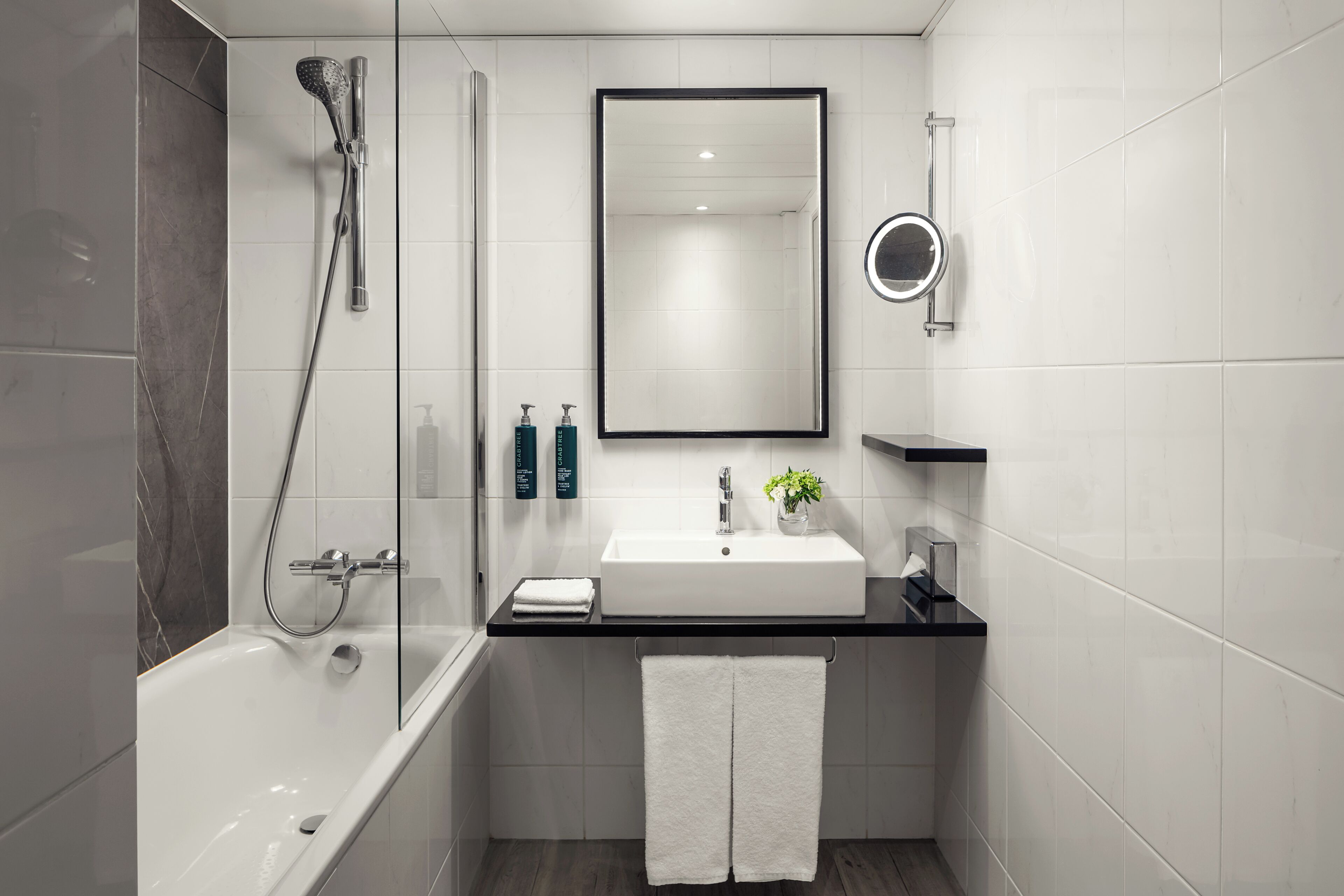 Ein modernes Badezimmer mit einer Badewanne, einer Dusche, einem Waschbecken mit Spiegel und einem Handtuchhalter.