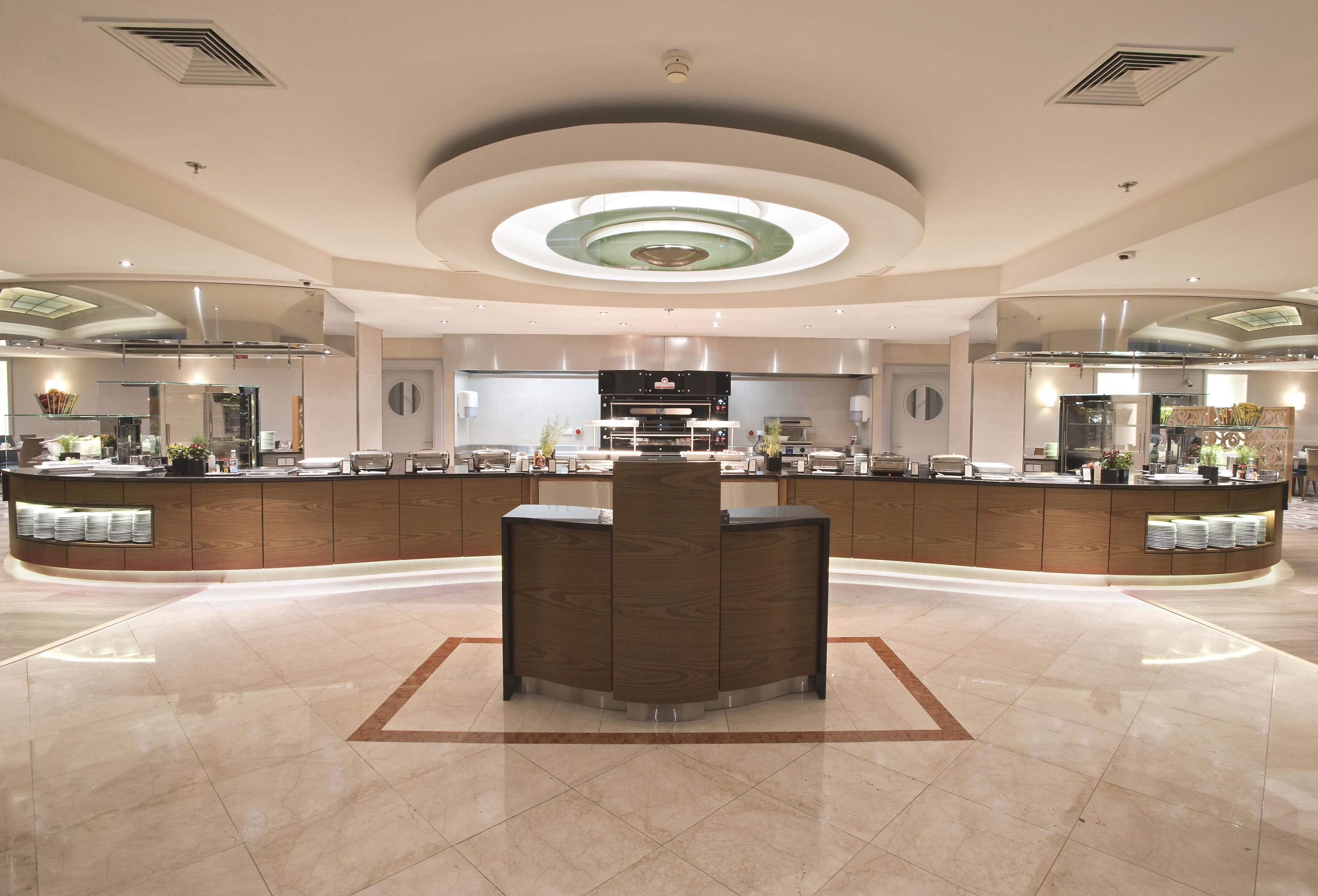 A spacious lobby with a central reception desk, a large circular skylight, and a modern kitchen area.
