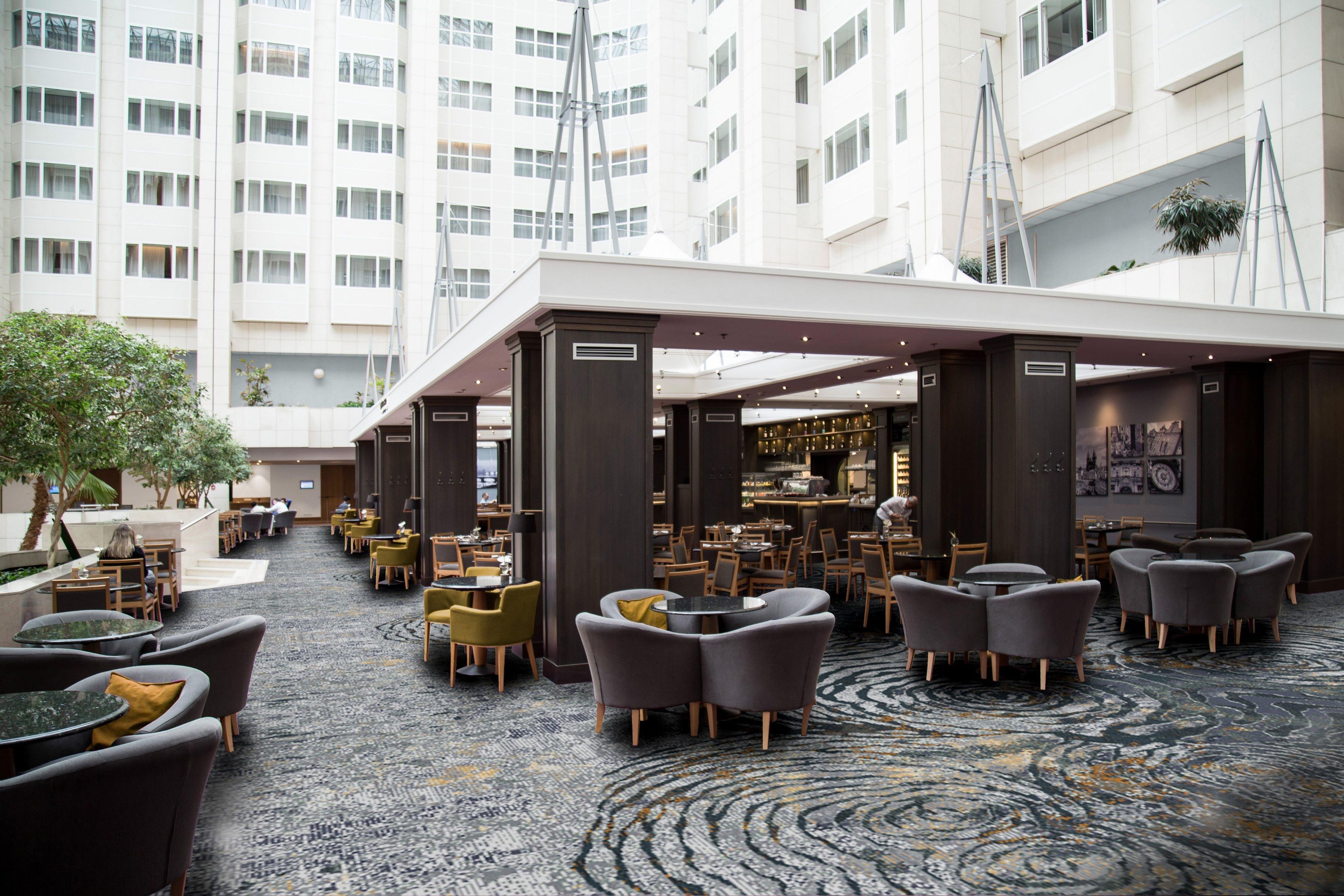 A hotel lobby with a bar area, seating arrangements, and a view of the building's exterior.