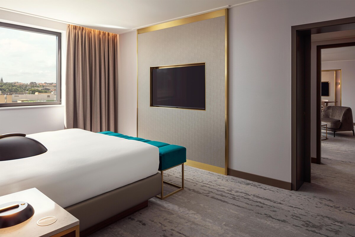 A hotel room with a bed, a desk, a chair, a TV, and a view of the city.