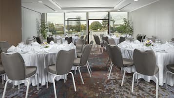 A conference room with multiple tables set for dining, chairs, and a carpeted floor.