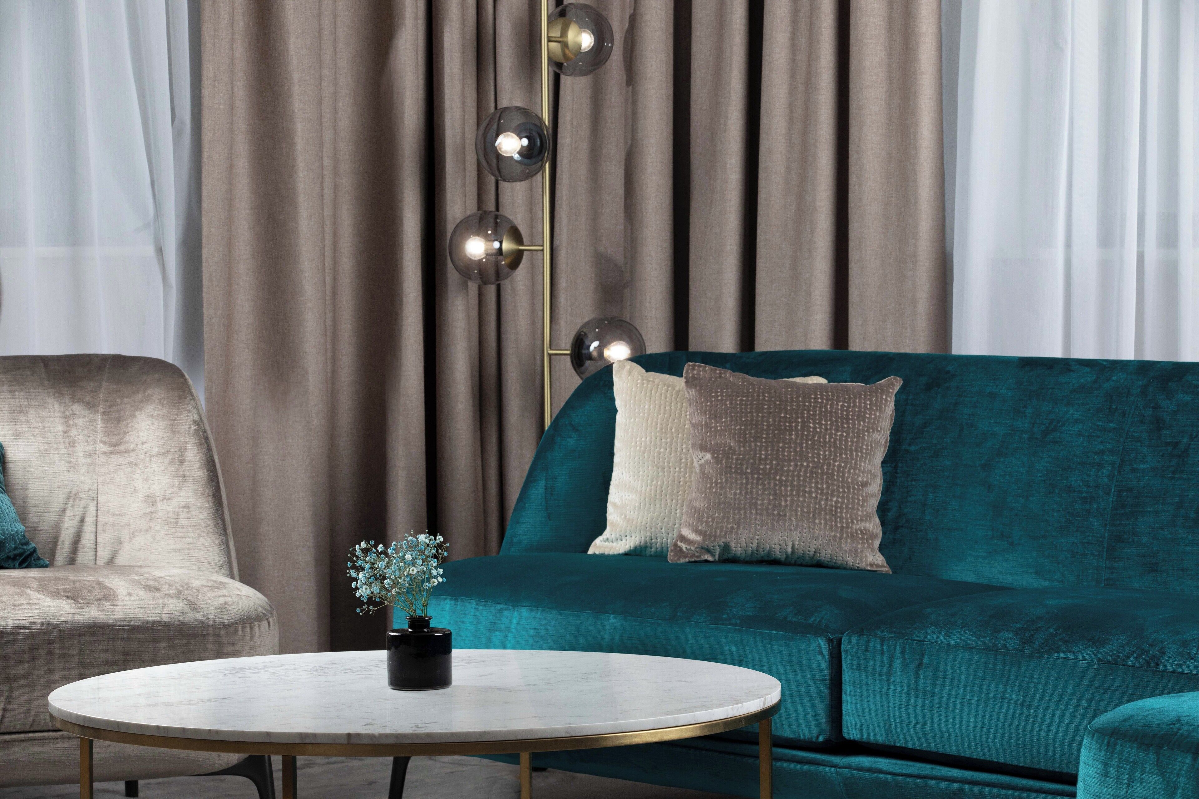 Een moderne woonkamer met een blauwgroene bank, een ronde salontafel en een hoge staande lamp.