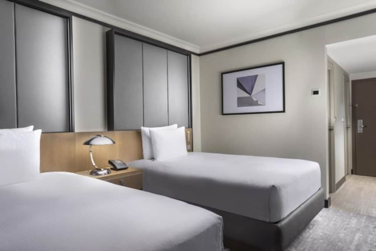 Habitación de hotel con dos camas, una mesita de noche con lámpara, teléfono y un cuadro en la pared.