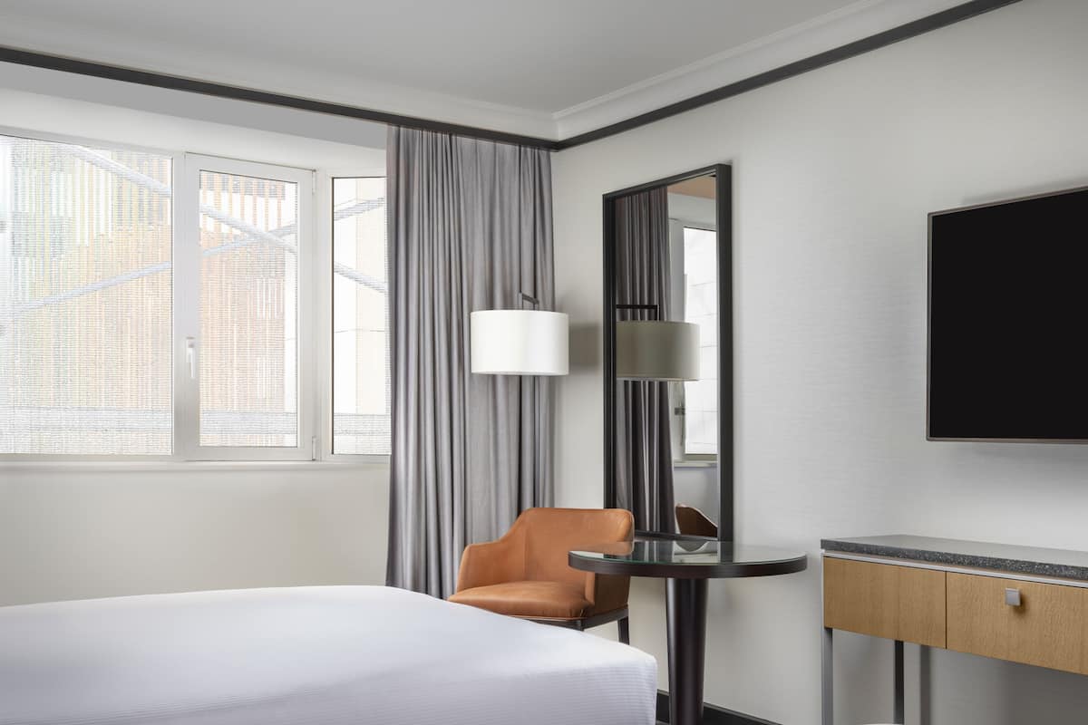 Ett hotellrum med en säng, en stol, ett skrivbord med en spegel och en tv.
