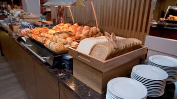 Un bufé con diversas opciones de panadería y panes, acompañado de platos blancos apilados.