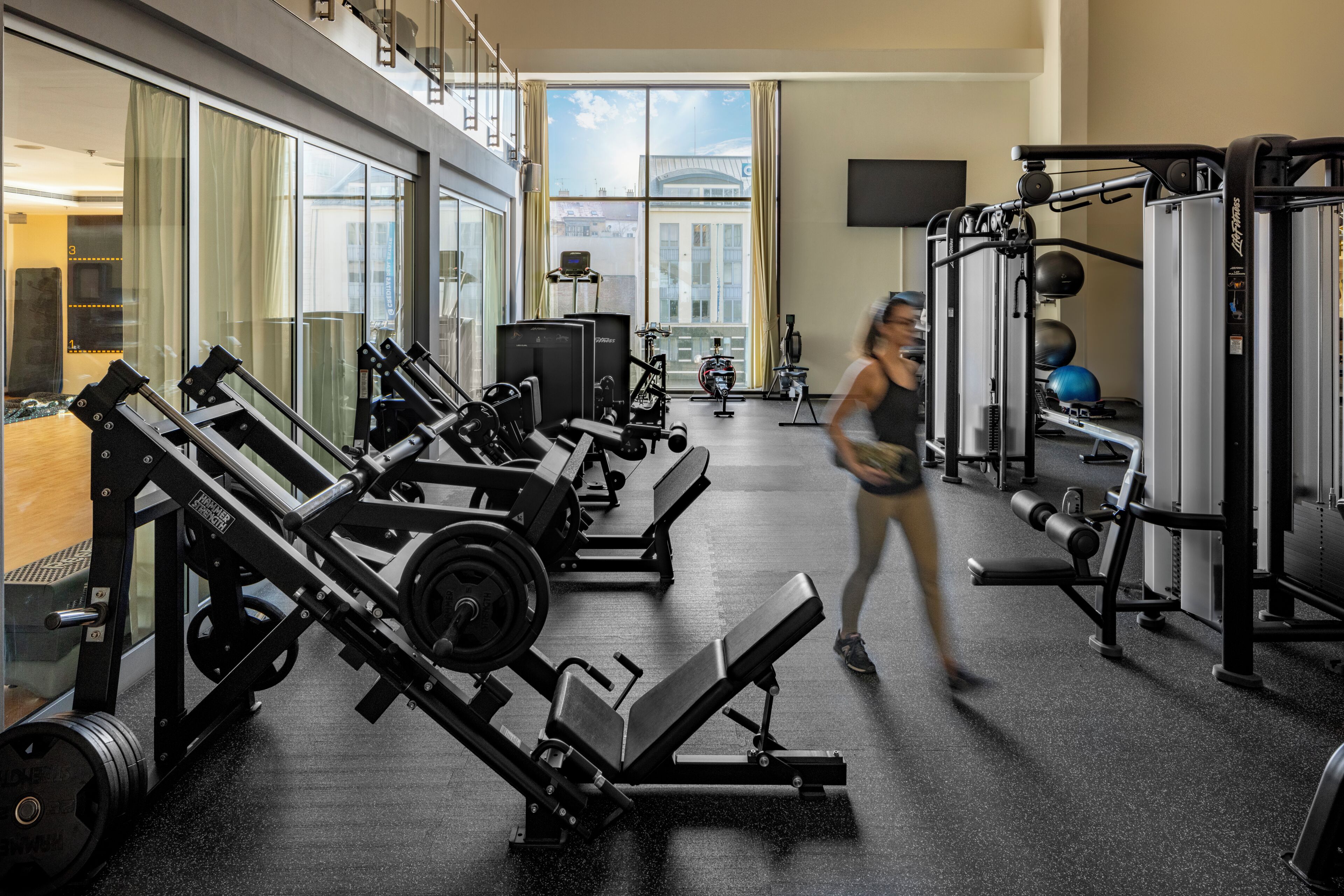 Ein Fitnessstudio mit Kraftgeräten, Laufbändern und einem großen Fenster mit Blick auf die Stadt.