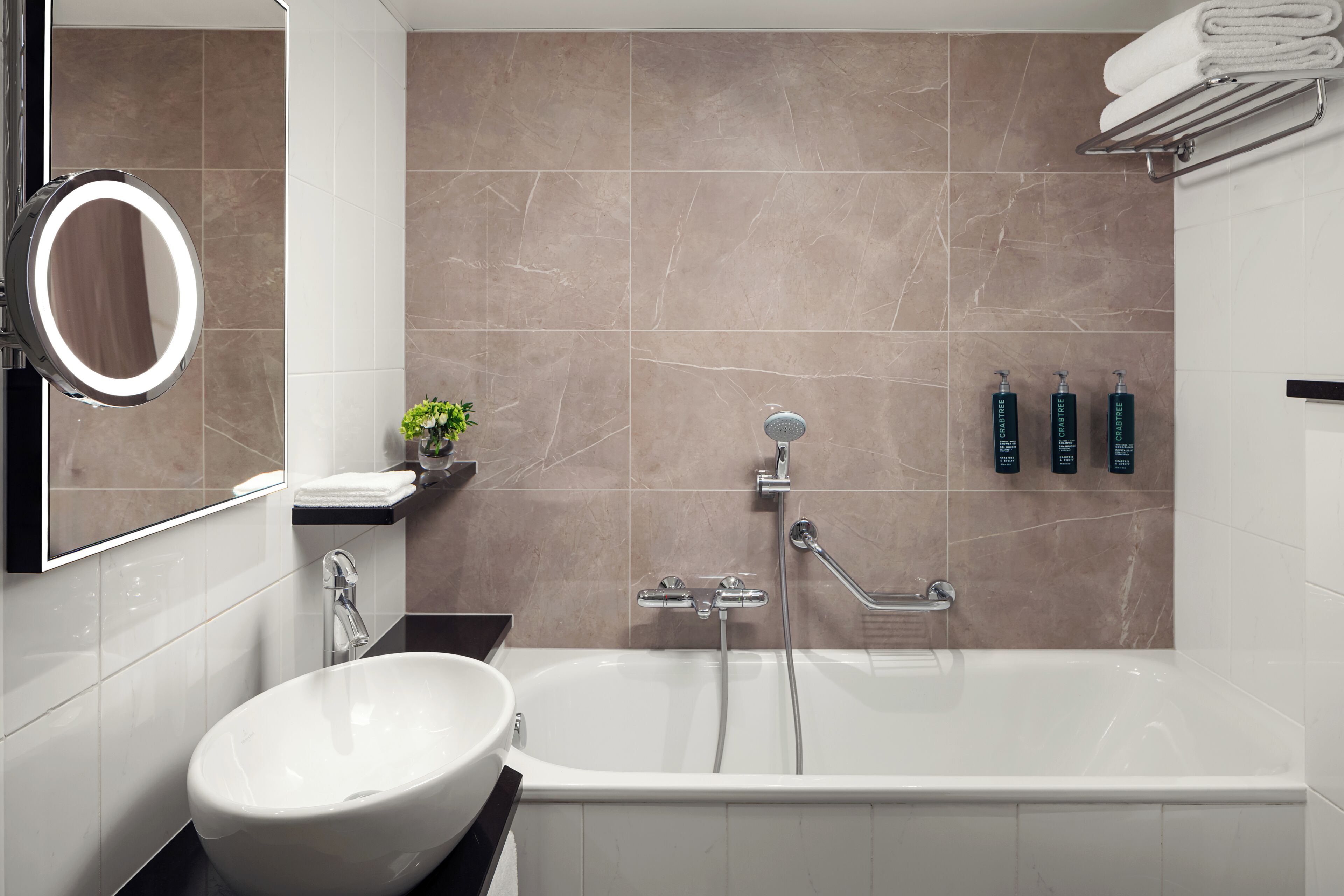 A modern bathroom with a freestanding bathtub, a round mirror, a sink, and a small plant.