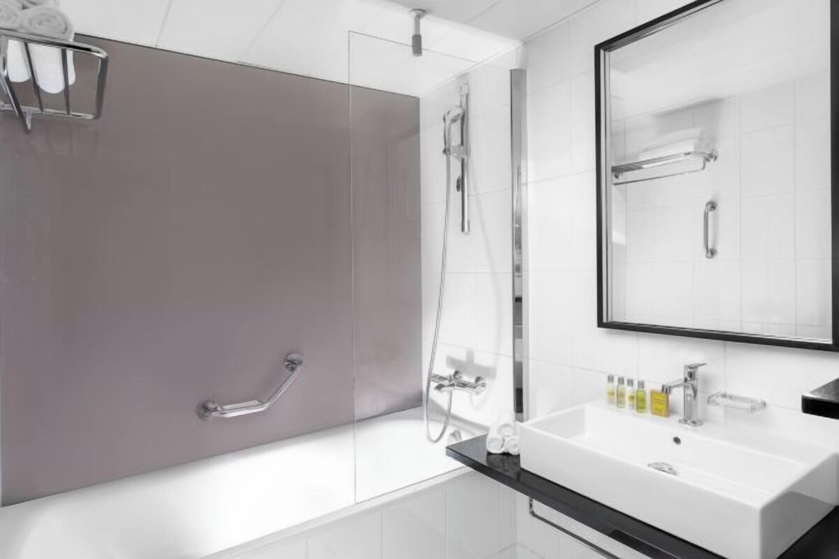 A modern bathroom with a walk-in shower, a large mirror, and a white sink with toiletries.
