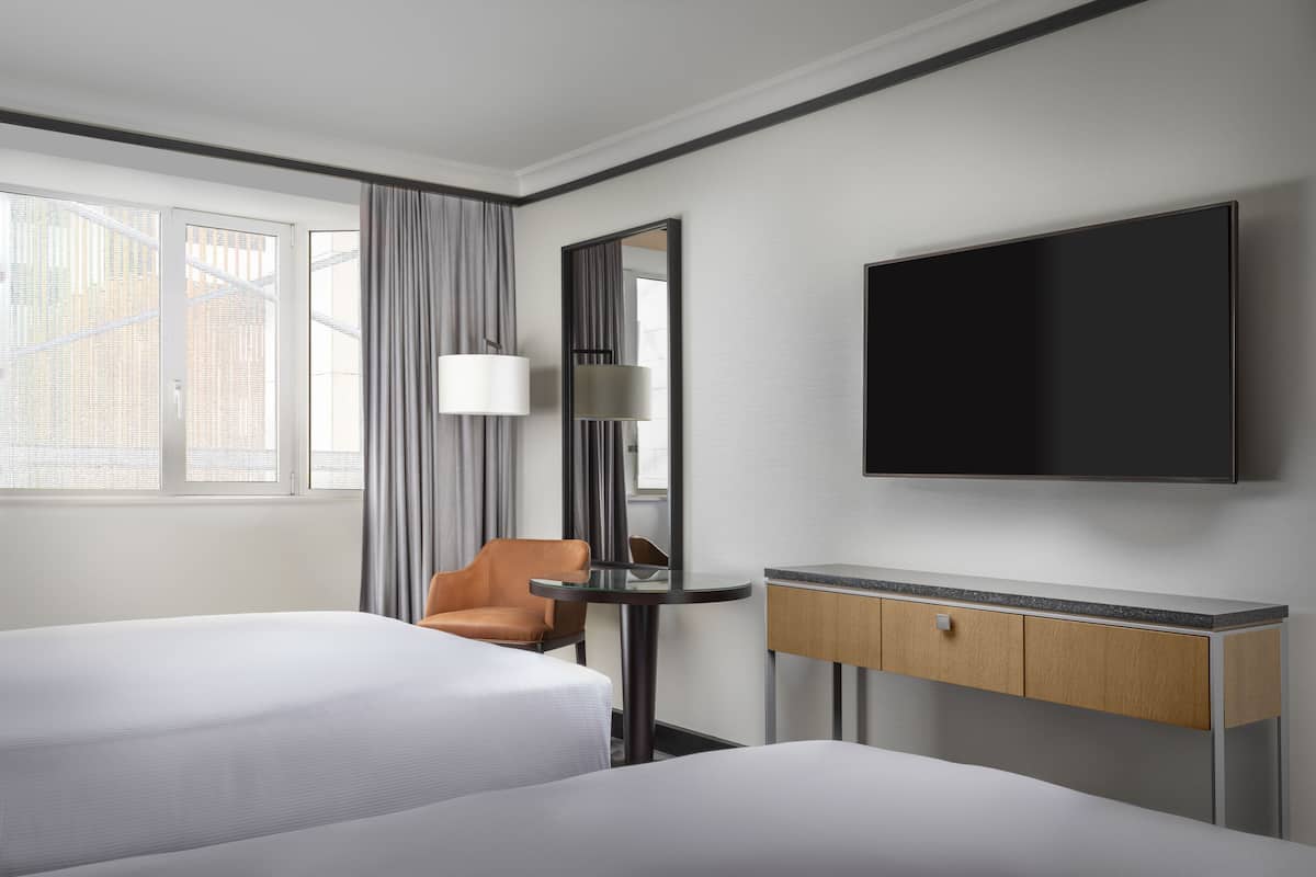 Ett hotellrum med två sängar, ett skrivbord, en stol, en tv och ett fönster med gardiner.