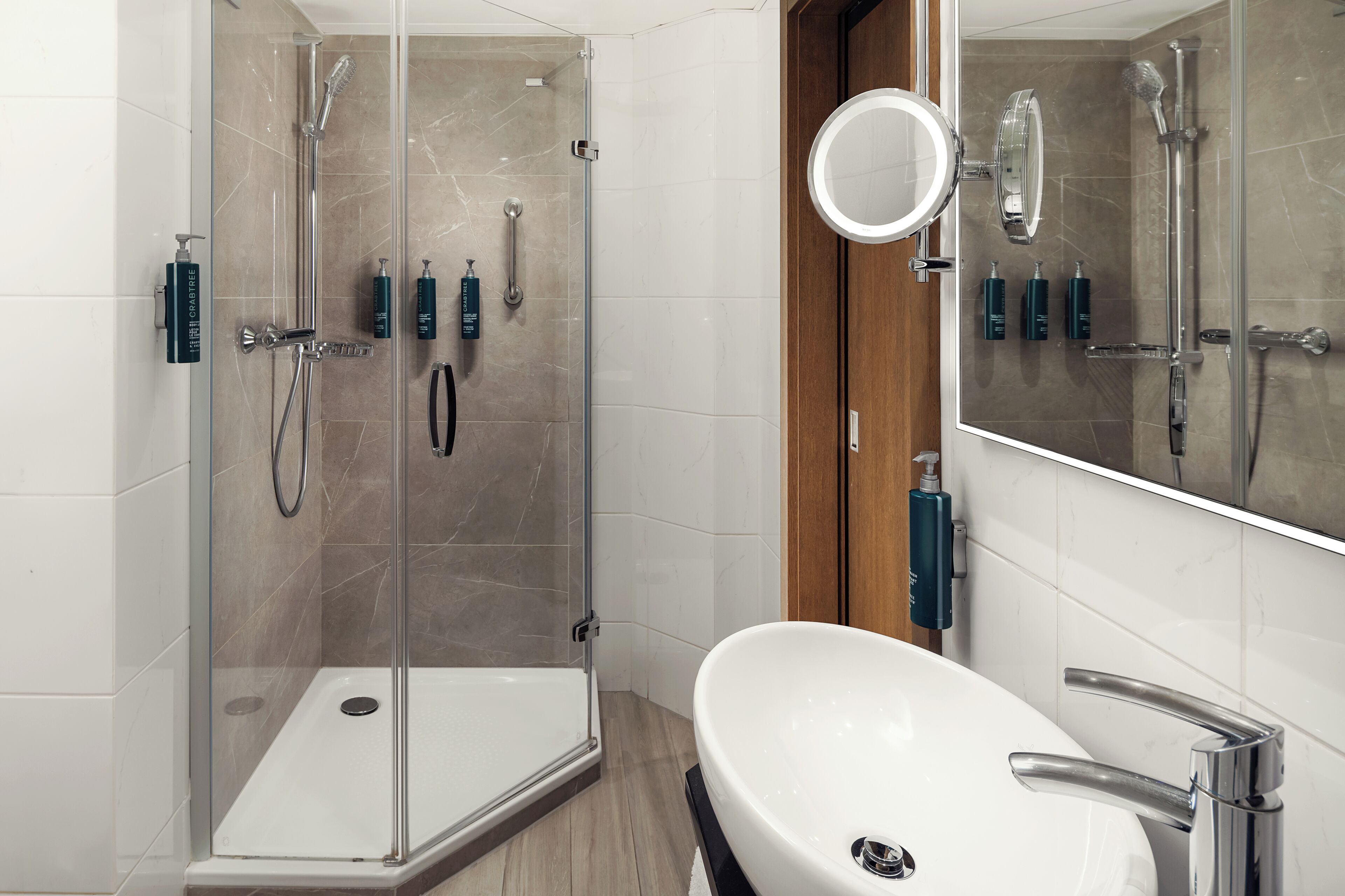Een moderne badkamer met een douchecabine van glas, een witte wastafel en een spiegel.
