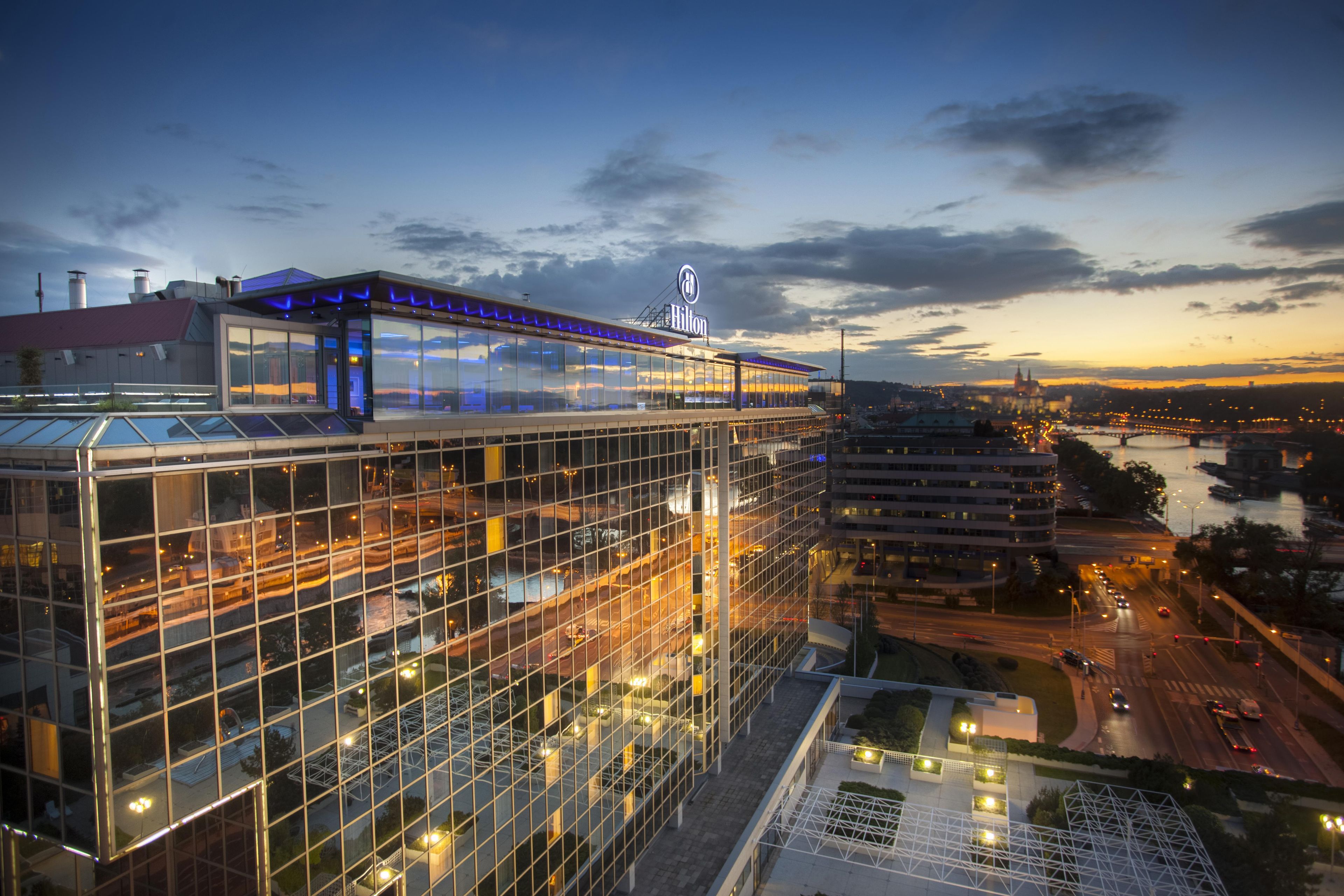 A modern hotel with a glass facade, a rooftop terrace, and a view of the cityscape.