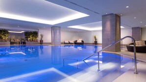 Une piscine intérieure moderne, dotée d’une eau claire, d’une paroi en verre et d’un espace détente avec un canapé et des fauteuils.