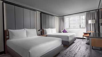 Habitación de hotel con dos camas, un escritorio, una silla, una lámpara y un ventanal con cortinas.