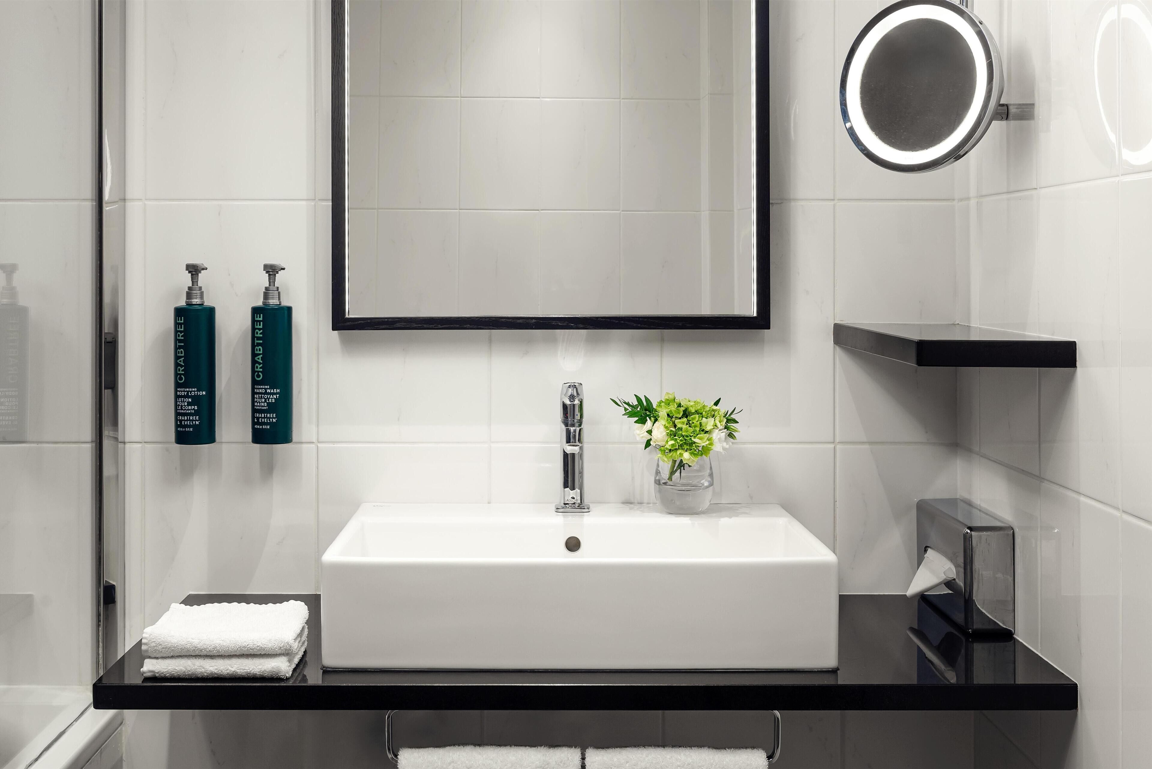 A modern bathroom with a white sink, a mirror, and two green bottles on the wall.