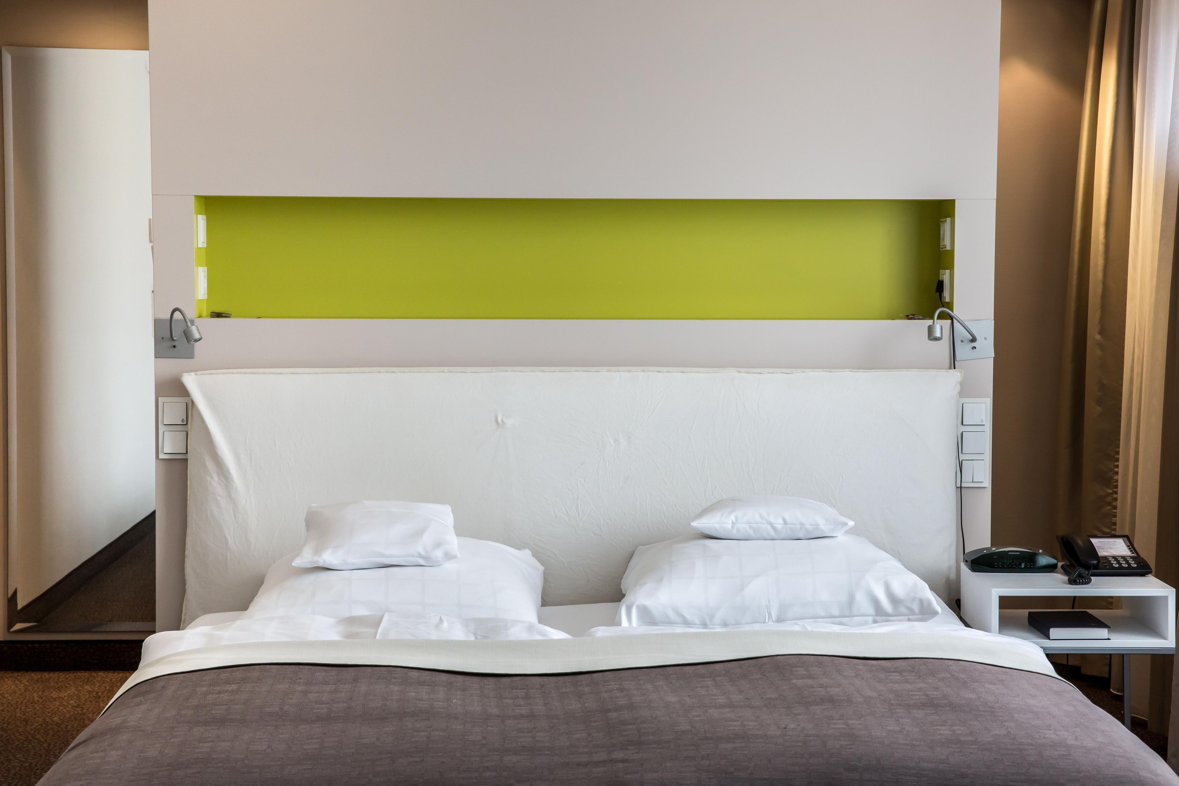 Ein Hotelzimmer mit einem großen Bett, zwei Kissen, einem Nachttisch mit Telefon und einer Wand in Grünton.