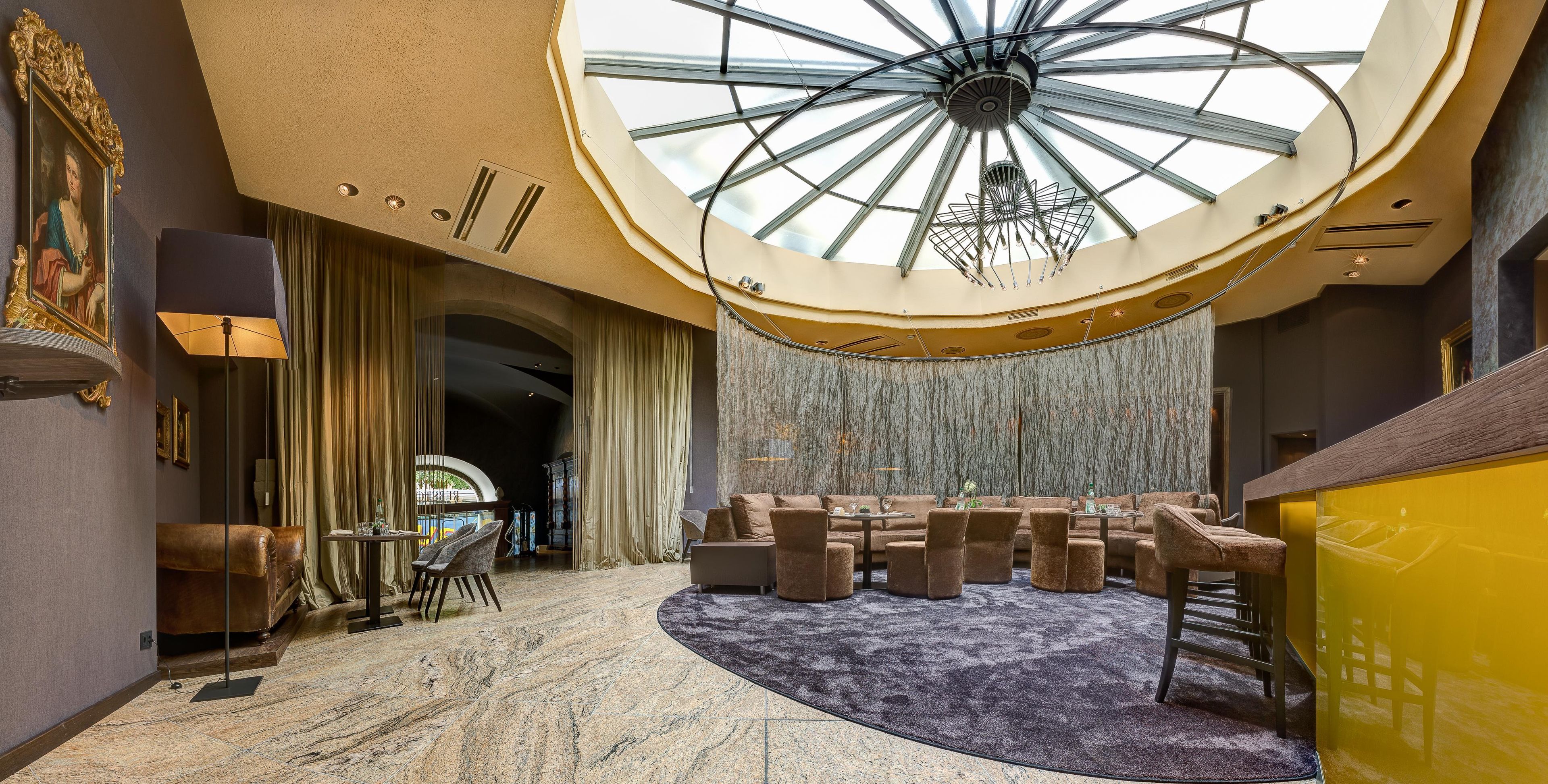 Eine geräumige Lobby mit hoher Decke, einer zentralen Sitzgruppe und einer imposanten Treppe.