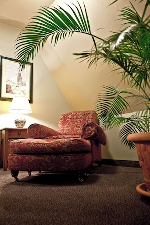 A corner room with a red patterned armchair, a potted plant, and a lamp on a nightstand.