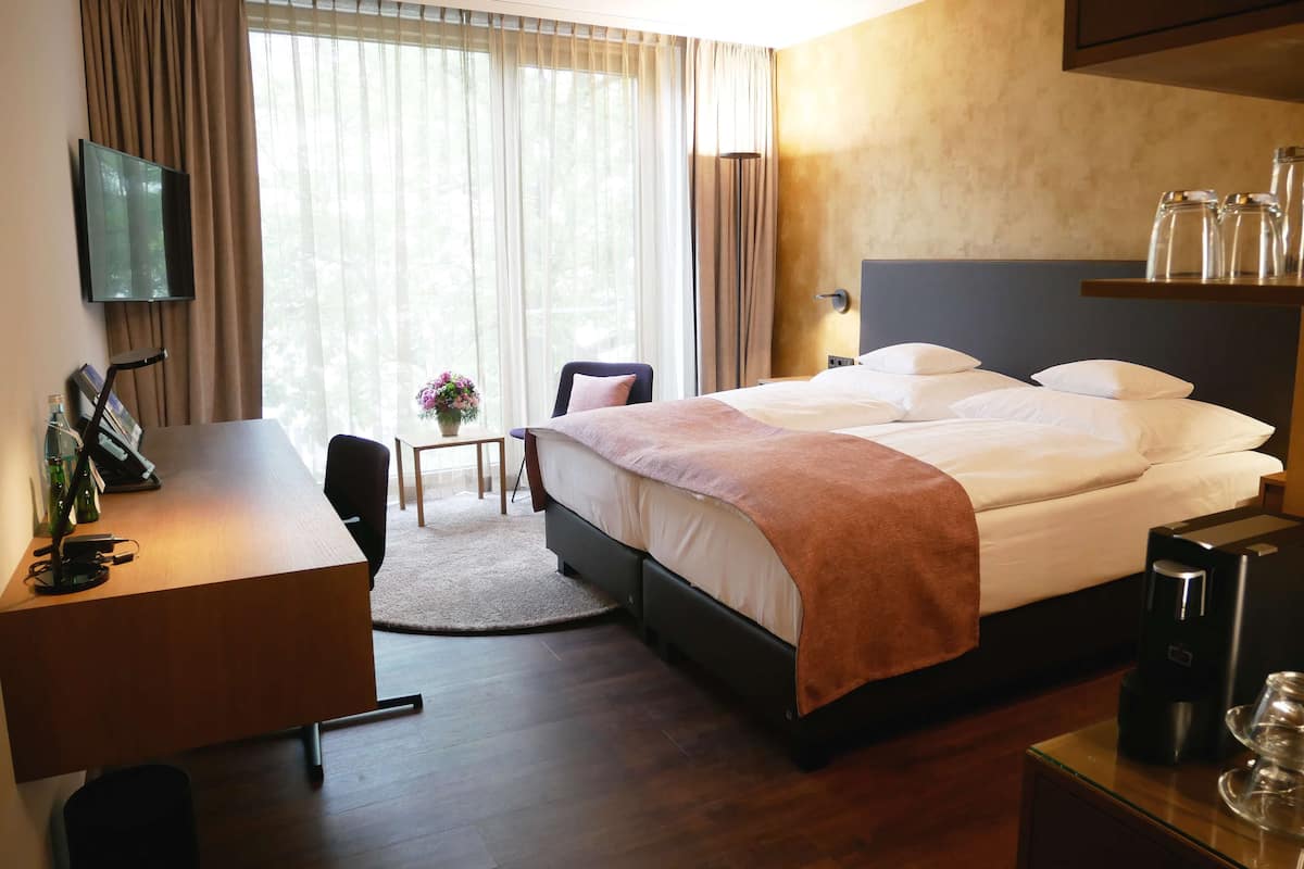 A hotel room with a bed, desk, chair, and a small table with a vase of flowers.