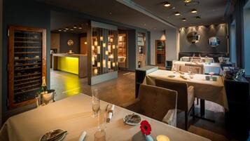 Interior de un restaurante con zona de bar, mesas dispuestas para comensales y una exhibición de vinos.