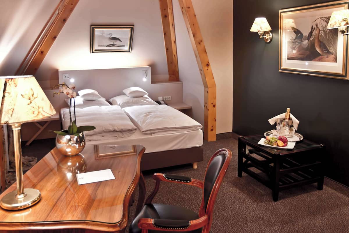 A bedroom with a bed, bedside table, lamp, chair, and a small table with fruit.