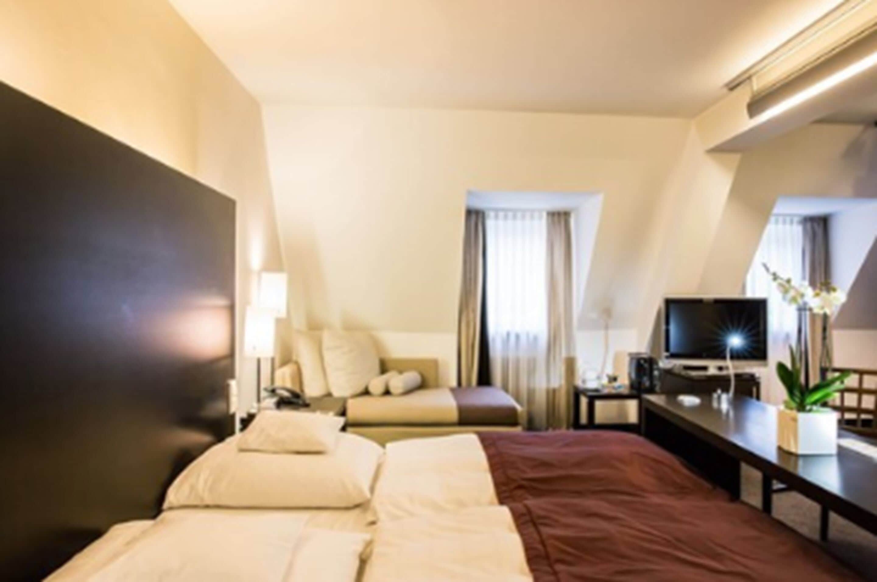 Hotellihuone, jossa on sänky, työpöytä, jossa on televisio, tuoli ja ikkuna, jossa on verhot.