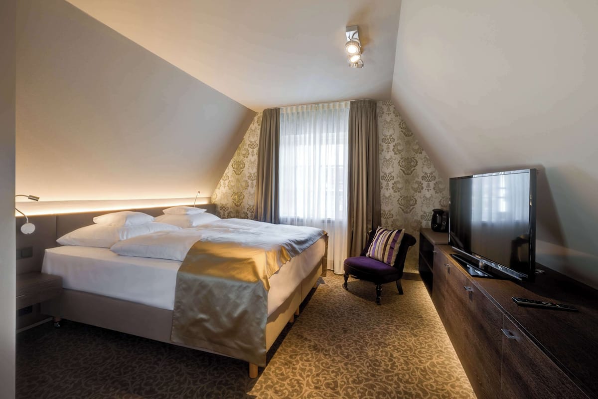 A hotel room with a bed, a TV, a chair, and a desk.