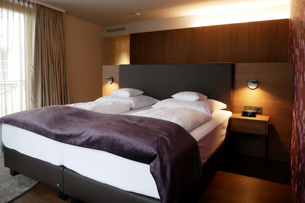 A modern hotel room with a large bed, two bedside tables, and a headboard with built-in lighting.